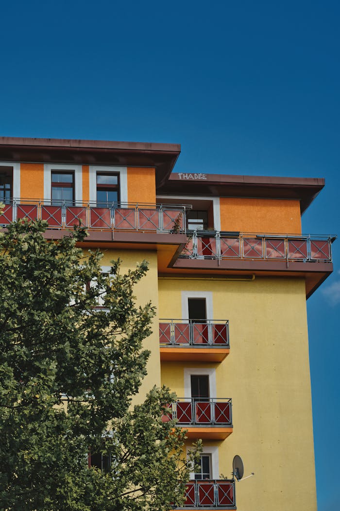 Bright yellow and orange apartment building in Berlin with sunny blue sky and green tree.